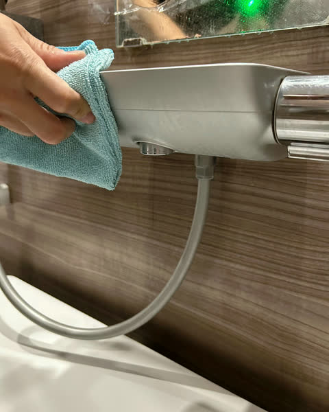 浴室のシャワー水栓を拭き上げるスタッフの手元
